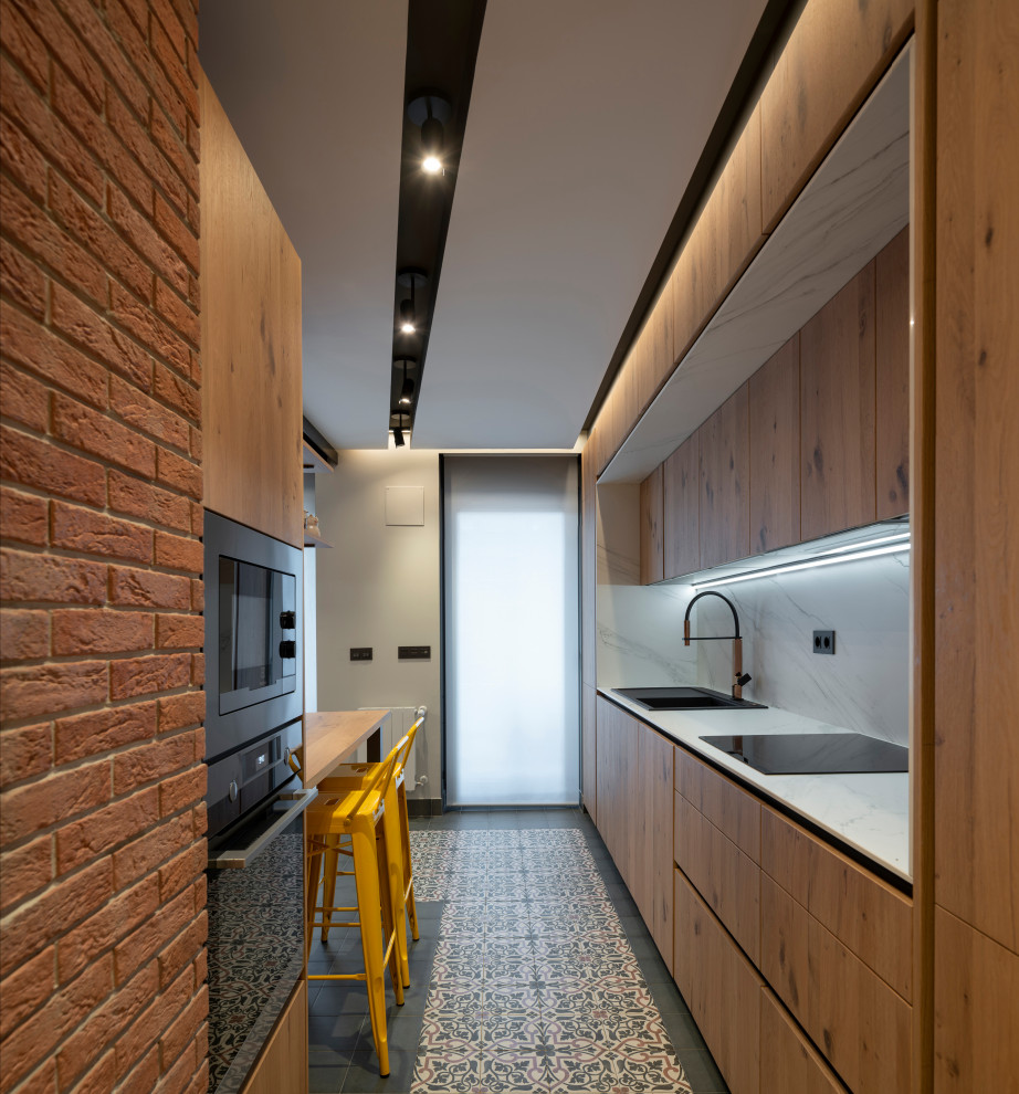Mid-sized contemporary galley kitchen in Bilbao with a drop-in sink, flat-panel cabinets, medium wood cabinets, white splashback, porcelain splashback, black appliances, a peninsula, multi-coloured floor and white benchtop.