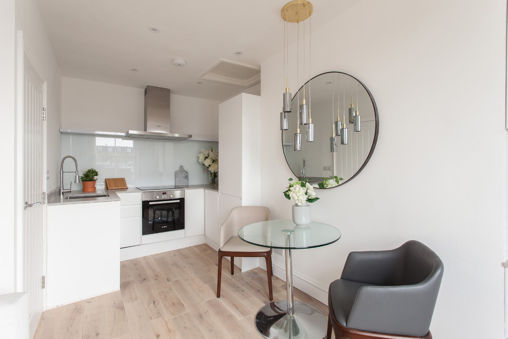Design ideas for a contemporary u-shaped open plan kitchen in London with an undermount sink, flat-panel cabinets, white cabinets, glass sheet splashback, light hardwood floors and beige floor.
