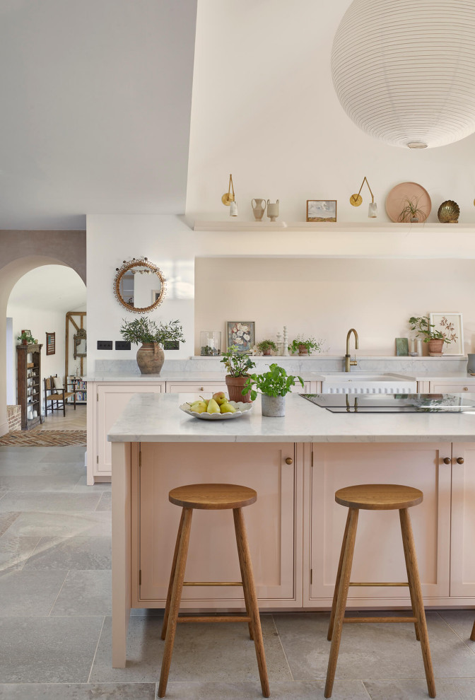 Large farmhouse grey and pink single-wall open plan kitchen in London with a belfast sink, shaker cabinets, pink cabinets, quartz worktops, pink splashback, black appliances, ceramic flooring, an island, multi-coloured floors, grey worktops and a vaulted ceiling.