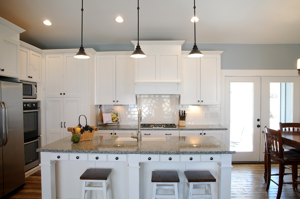 This is an example of a large arts and crafts u-shaped open plan kitchen in Salt Lake City with a farmhouse sink, shaker cabinets, white cabinets, granite benchtops, white splashback, subway tile splashback, stainless steel appliances, dark hardwood floors, with island and brown floor.