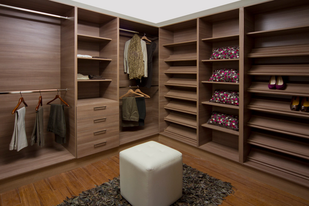 Modelo de armario vestidor unisex actual de tamaño medio con armarios con paneles lisos, puertas de armario de madera oscura y suelo de madera en tonos medios