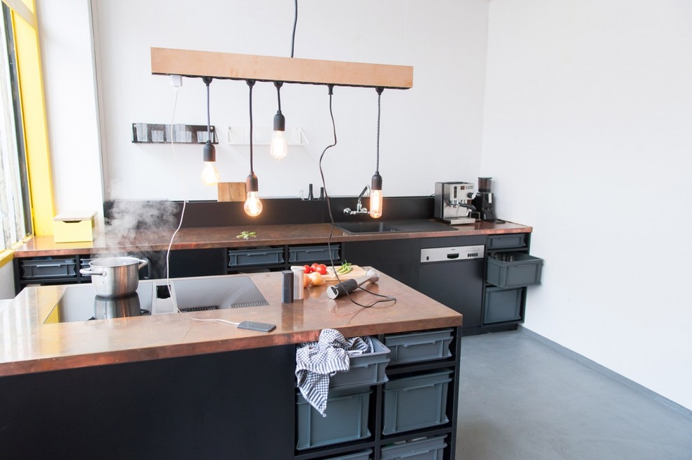 Photo of a mid-sized contemporary single-wall open plan kitchen in Berlin with a drop-in sink, black cabinets, copper benchtops, black appliances, concrete floors, with island and white splashback.