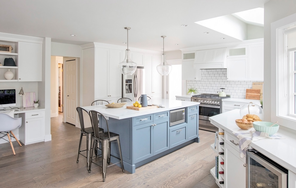 This is an example of a large beach style l-shaped open plan kitchen in Vancouver with a farmhouse sink, shaker cabinets, white cabinets, quartz benchtops, white splashback, ceramic splashback, stainless steel appliances, dark hardwood floors, with island and brown floor.