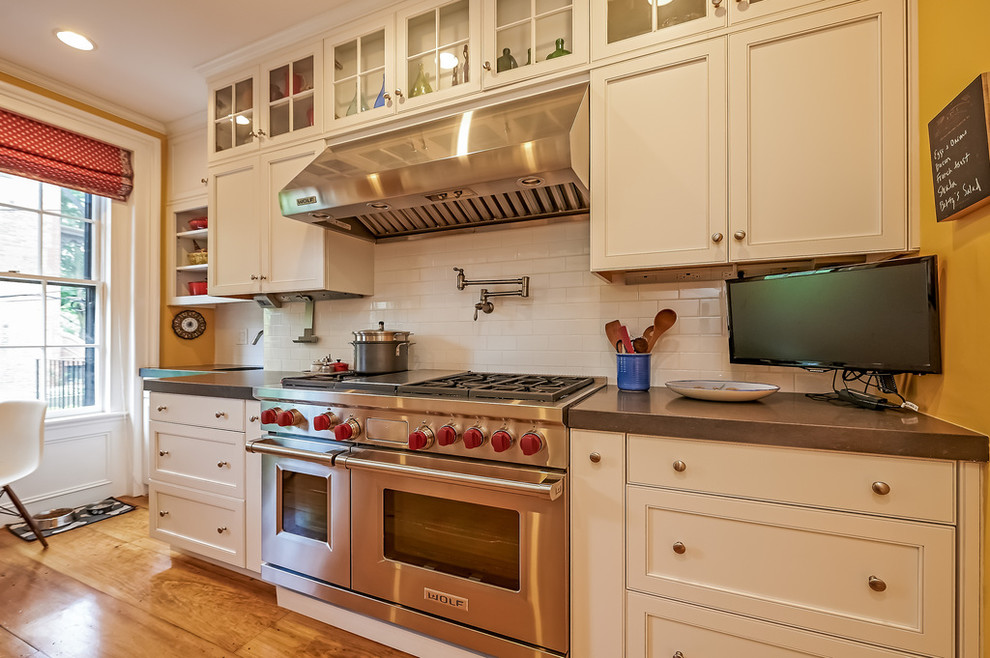 Small transitional u-shaped medium tone wood floor and beige floor enclosed kitchen photo in Boston with recessed-panel cabinets, white cabinets, solid surface countertops, white backsplash, subway tile backsplash, stainless steel appliances, no island and an undermount sink