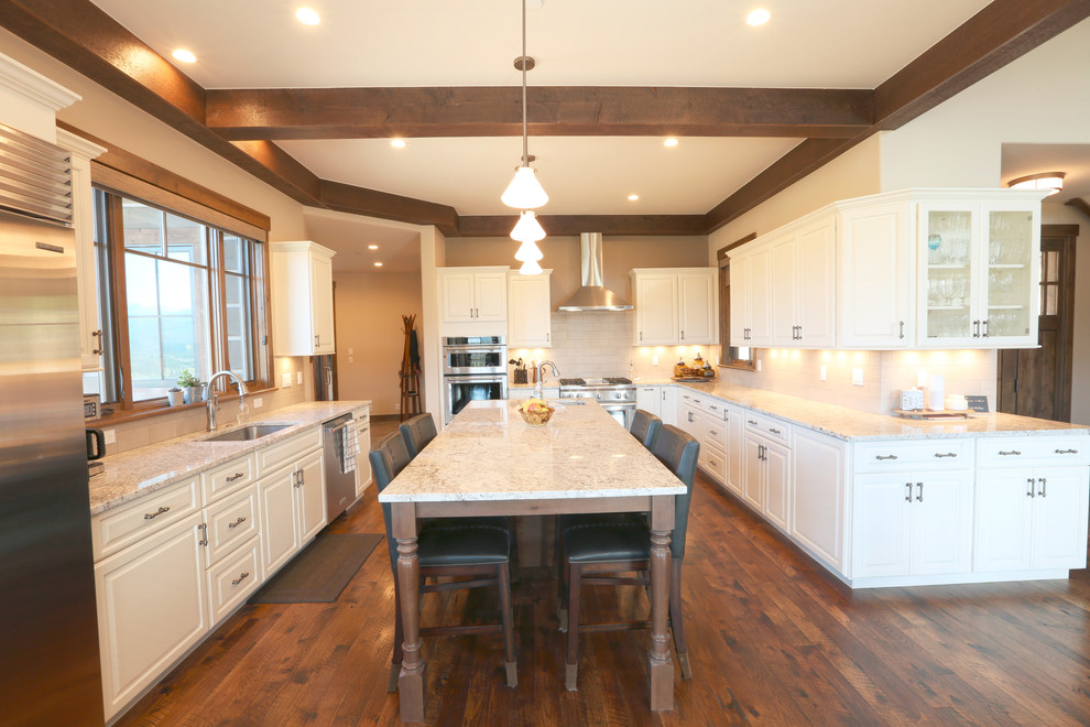 Photo of a large country u-shaped open plan kitchen in Denver with an undermount sink, flat-panel cabinets, white cabinets, granite benchtops, white splashback, stone tile splashback, stainless steel appliances, dark hardwood floors, with island, brown floor and white benchtop.
