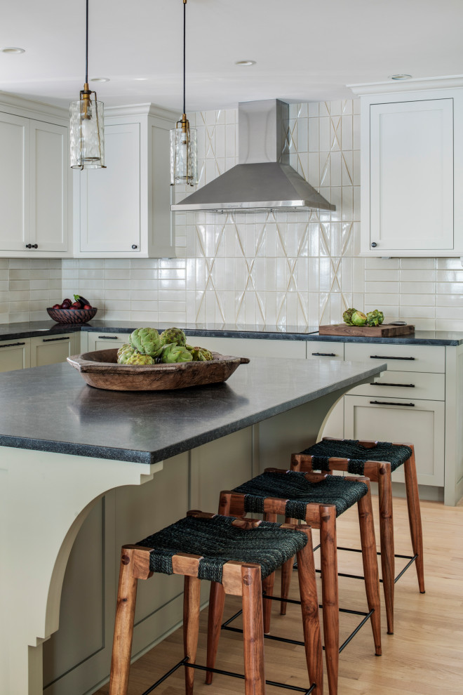 This is an example of a large beach style l-shaped open plan kitchen in Boston with an undermount sink, recessed-panel cabinets, green cabinets, soapstone benchtops, beige splashback, glass tile splashback, stainless steel appliances, light hardwood floors, with island and black benchtop.