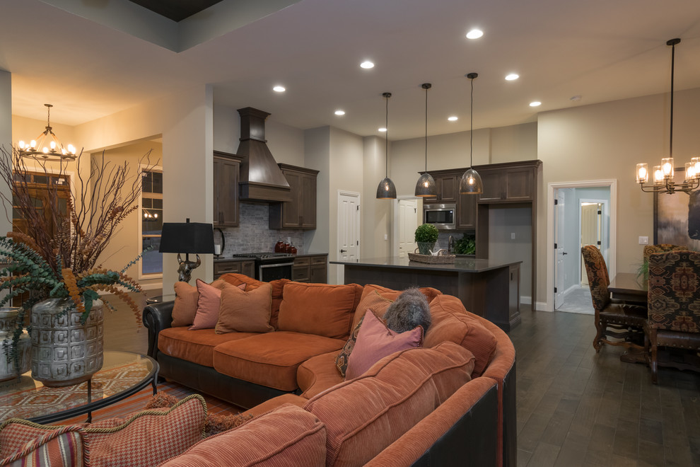 Open concept kitchen - large rustic galley medium tone wood floor and brown floor open concept kitchen idea with a single-bowl sink, shaker cabinets, brown cabinets, quartz countertops, gray backsplash, stone tile backsplash, stainless steel appliances and an island