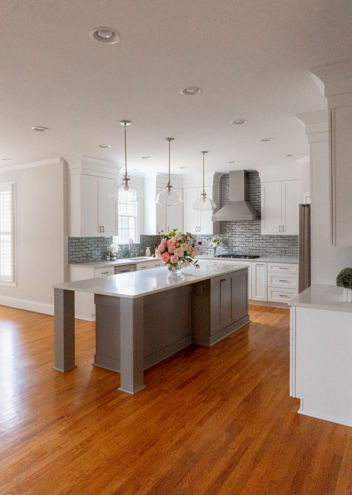 Foto på ett mellanstort funkis vit kök, med en undermonterad diskho, skåp i shakerstil, vita skåp, bänkskiva i kvarts, grått stänkskydd, glaspanel som stänkskydd, rostfria vitvaror, mellanmörkt trägolv, en köksö och orange golv