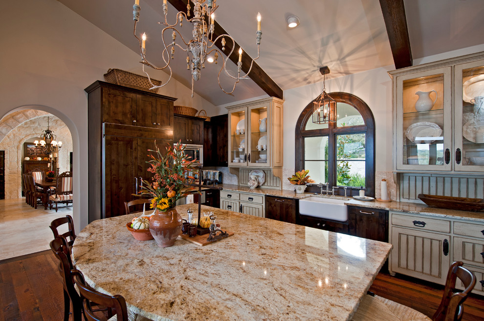 Photo of a large mediterranean u-shaped eat-in kitchen in Austin with a farmhouse sink, glass-front cabinets, dark wood cabinets, granite benchtops, white splashback, panelled appliances, dark hardwood floors, with island and brown floor.