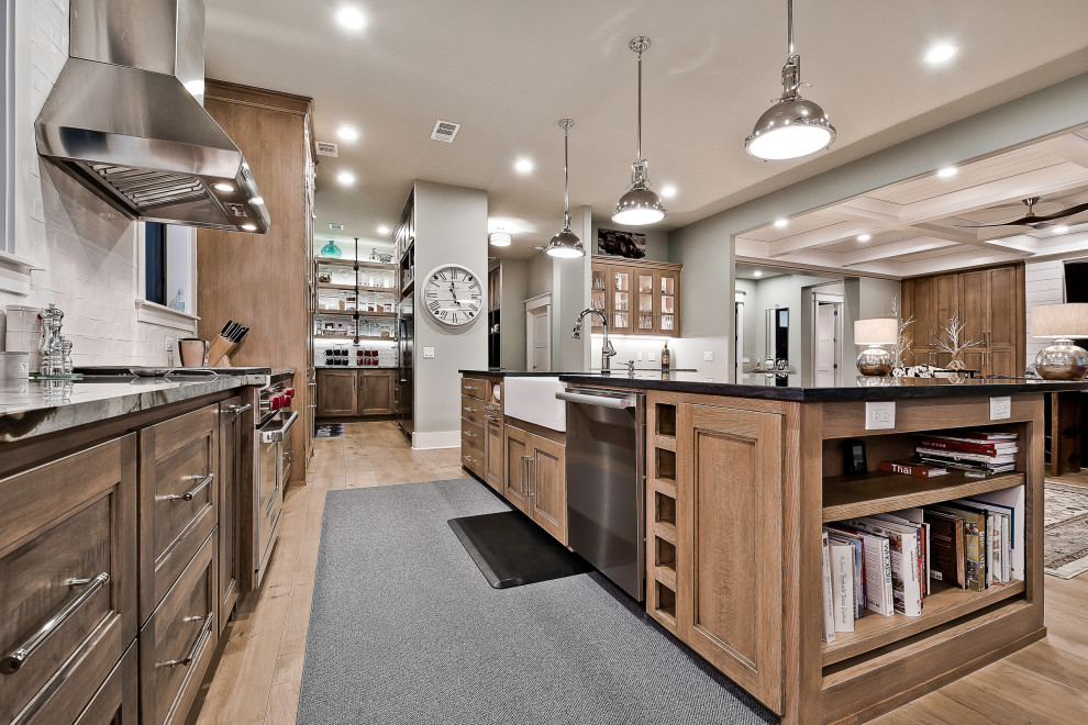This is an example of an expansive modern kitchen in Other with a farmhouse sink, recessed-panel cabinets, brown cabinets, granite benchtops, white splashback, porcelain splashback, stainless steel appliances, light hardwood floors, with island and black benchtop.