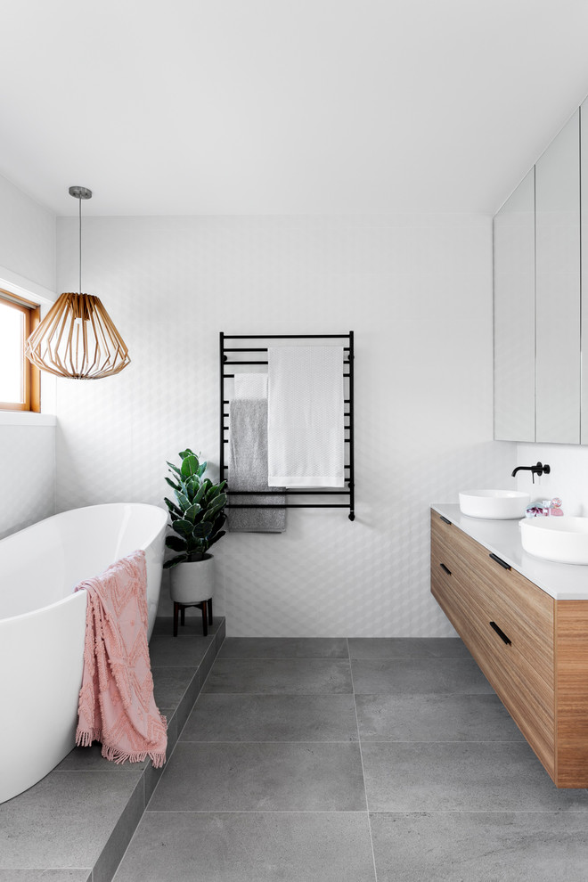 Photo of a contemporary bathroom in Melbourne with flat-panel cabinets, medium wood cabinets, a freestanding tub, white tile, a vessel sink, grey floor and grey benchtops.
