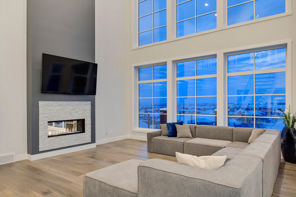 Large contemporary open concept living room in Calgary with white walls, light hardwood floors, a standard fireplace, a tile fireplace surround and a wall-mounted tv.