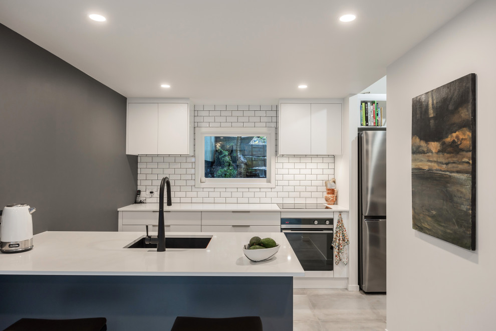 Small modern galley kitchen pantry in Auckland with a submerged sink, flat-panel cabinets, white cabinets, engineered stone countertops, white splashback, metro tiled splashback, porcelain flooring, a breakfast bar, grey floors and white worktops.