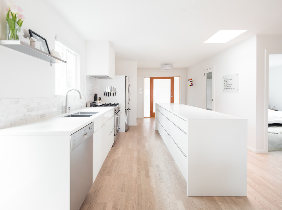 This is an example of a contemporary galley kitchen in Vancouver with an undermount sink, flat-panel cabinets, white cabinets, grey splashback, marble splashback, stainless steel appliances, light hardwood floors, with island and beige floor.