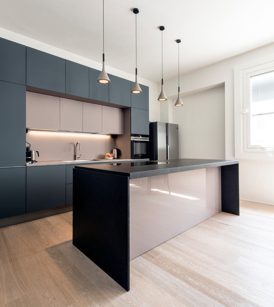 Design ideas for a large contemporary galley open plan kitchen in Milan with flat-panel cabinets, black appliances, light hardwood floors, with island, black benchtop, a drop-in sink, grey cabinets, marble benchtops, pink splashback, glass sheet splashback and beige floor.