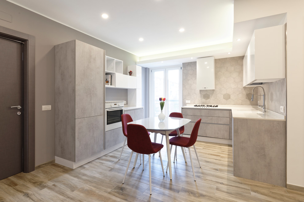 Design ideas for a mid-sized contemporary l-shaped eat-in kitchen in Milan with flat-panel cabinets, no island, grey cabinets, grey splashback, a drop-in sink, marble benchtops, ceramic splashback, stainless steel appliances, porcelain floors and brown floor.