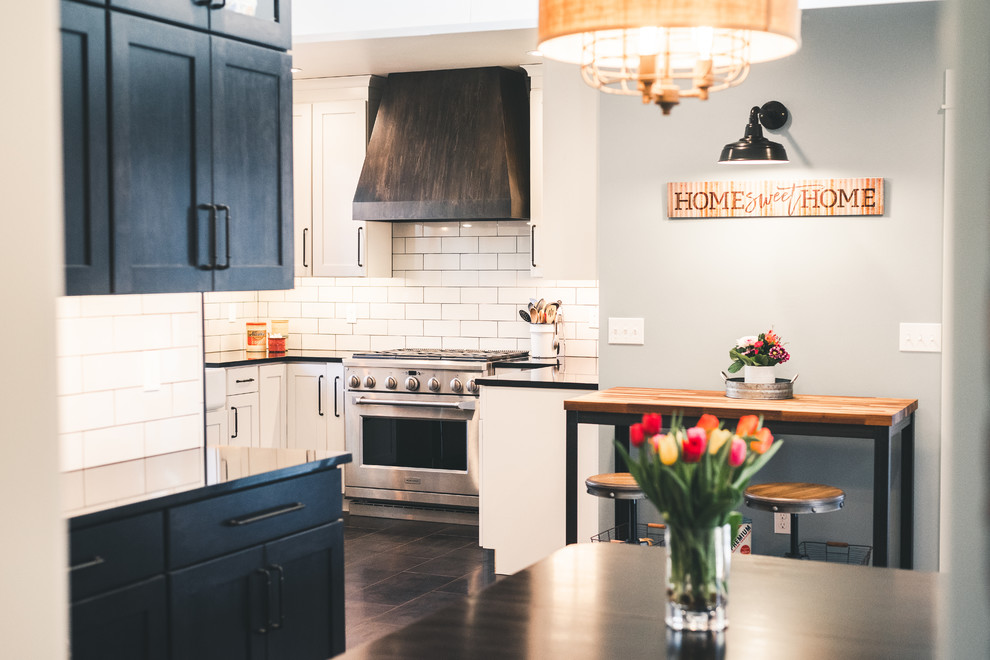 Photo of a large country u-shaped kitchen in Seattle with a farmhouse sink, shaker cabinets, white cabinets, quartz benchtops, white splashback, subway tile splashback, stainless steel appliances, black floor and black benchtop.