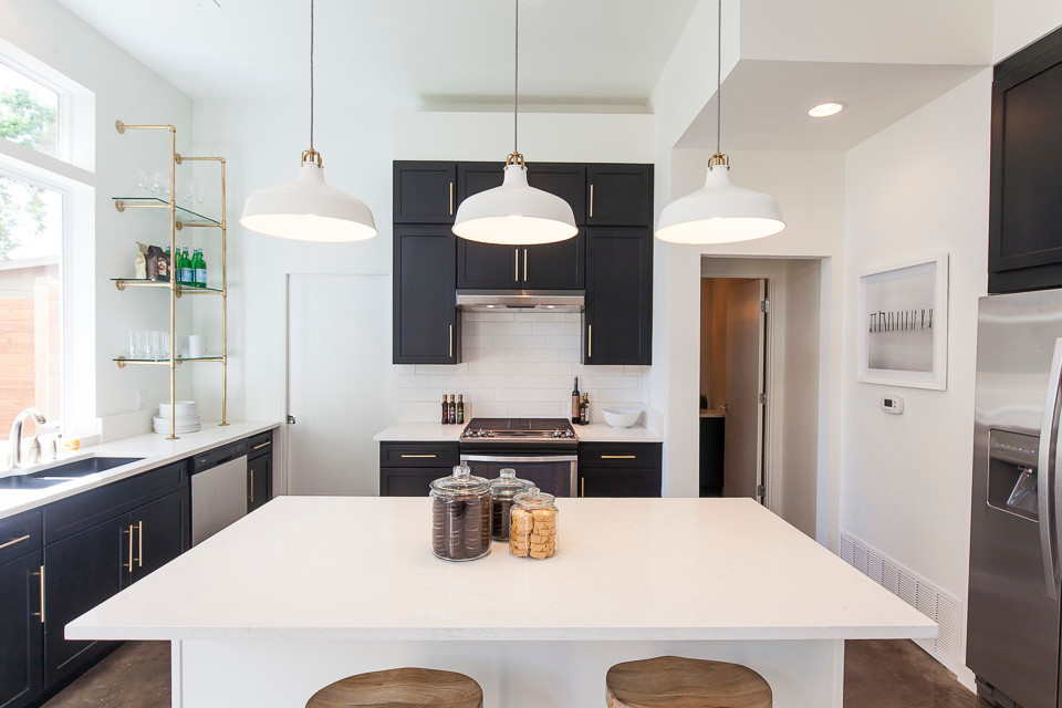 Design ideas for a large contemporary eat-in kitchen in Austin with a double-bowl sink, shaker cabinets, black cabinets, quartz benchtops, white splashback, subway tile splashback, stainless steel appliances, concrete floors and with island.