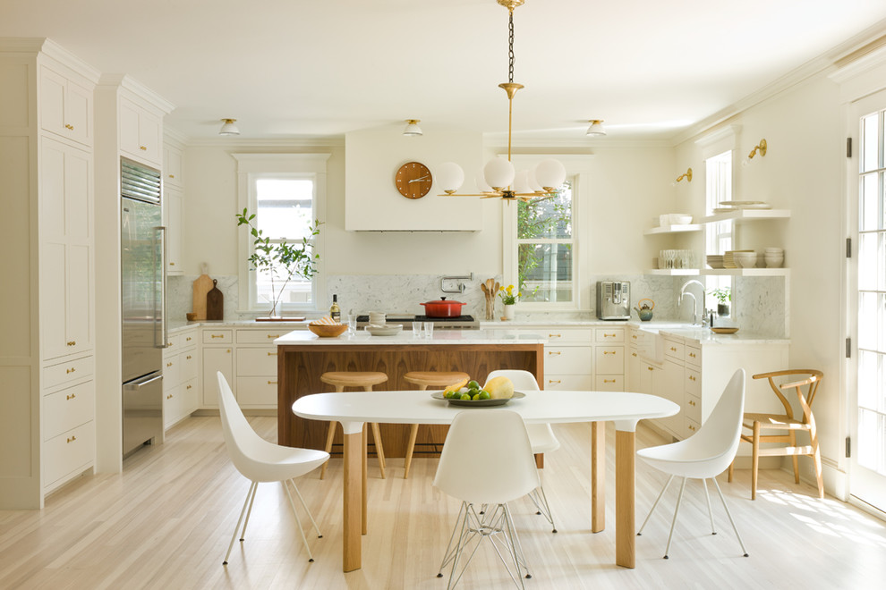 Photo of a transitional u-shaped kitchen in DC Metro with a farmhouse sink, shaker cabinets, white cabinets, white splashback, stone slab splashback, stainless steel appliances, light hardwood floors, with island, beige floor and white benchtop.