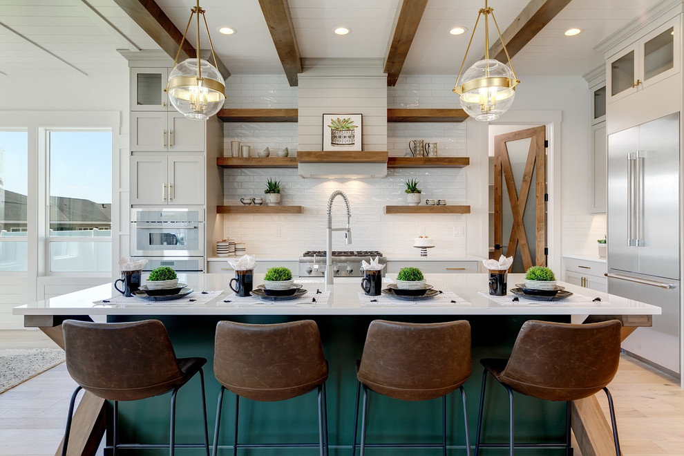 Design ideas for a large country l-shaped open plan kitchen in Boise with a farmhouse sink, shaker cabinets, white splashback, subway tile splashback, stainless steel appliances, light hardwood floors, with island, white benchtop, white cabinets, quartz benchtops and beige floor.