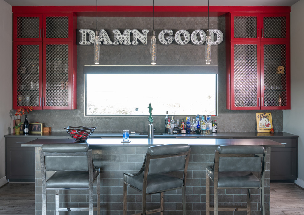 Design ideas for a mid-sized industrial galley seated home bar in Austin with an undermount sink, red cabinets, quartz benchtops, grey splashback, ceramic splashback, medium hardwood floors, grey floor, black benchtop and shaker cabinets.