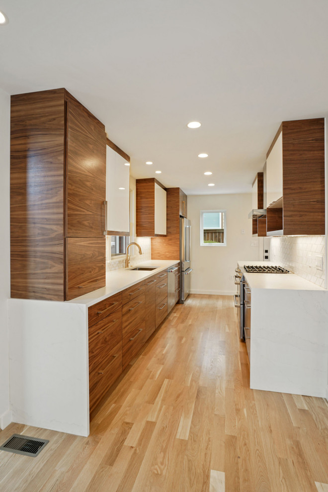 Photo of a small modern galley separate kitchen in DC Metro with an undermount sink, flat-panel cabinets, medium wood cabinets, quartz benchtops, white splashback, porcelain splashback, stainless steel appliances, light hardwood floors, no island, brown floor and white benchtop.