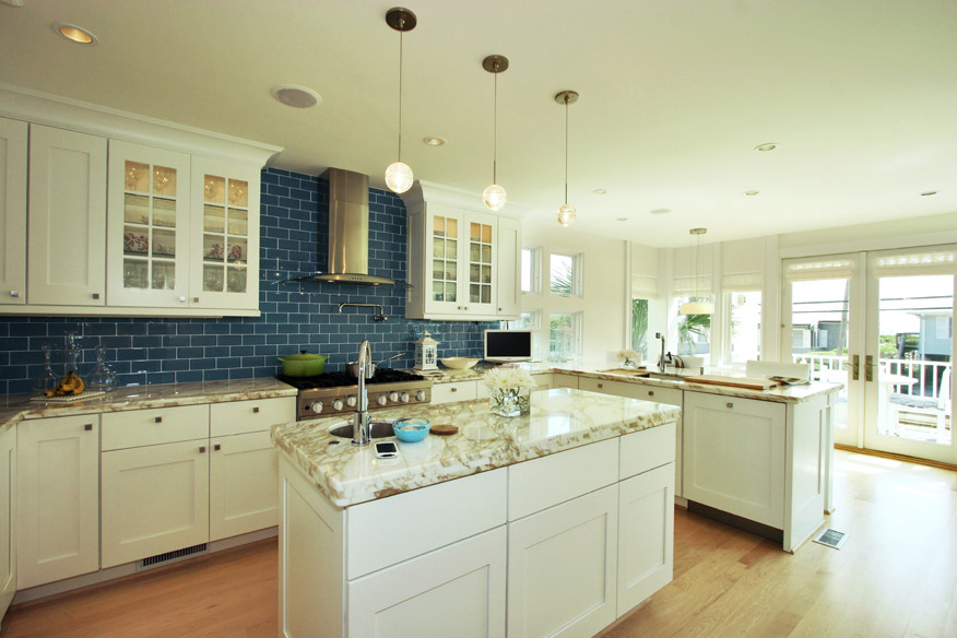 Inspiration for a large beach style u-shaped eat-in kitchen in Raleigh with a double-bowl sink, shaker cabinets, white cabinets, granite benchtops, blue splashback, subway tile splashback, stainless steel appliances, light hardwood floors and with island.