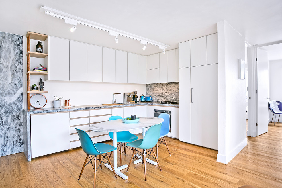 This is an example of a small contemporary l-shaped eat-in kitchen in Sydney with a double-bowl sink, flat-panel cabinets, white cabinets, marble benchtops, white splashback, marble splashback, black appliances, medium hardwood floors, no island, brown floor and grey benchtop.