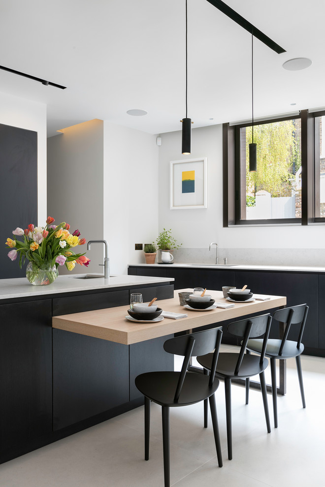 Large contemporary l-shaped eat-in kitchen in London with an undermount sink, flat-panel cabinets, black cabinets, marble benchtops, multi-coloured splashback, marble splashback, black appliances, ceramic floors, beige floor and multiple islands.