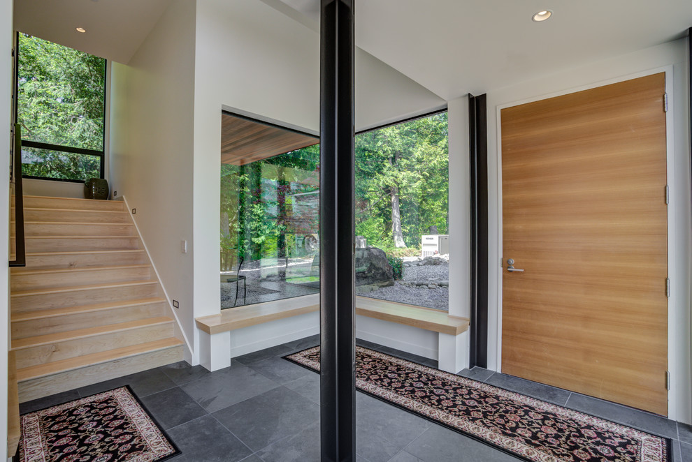 This is an example of a large modern foyer in Seattle with white walls, slate floors, a single front door, a light wood front door and black floor.