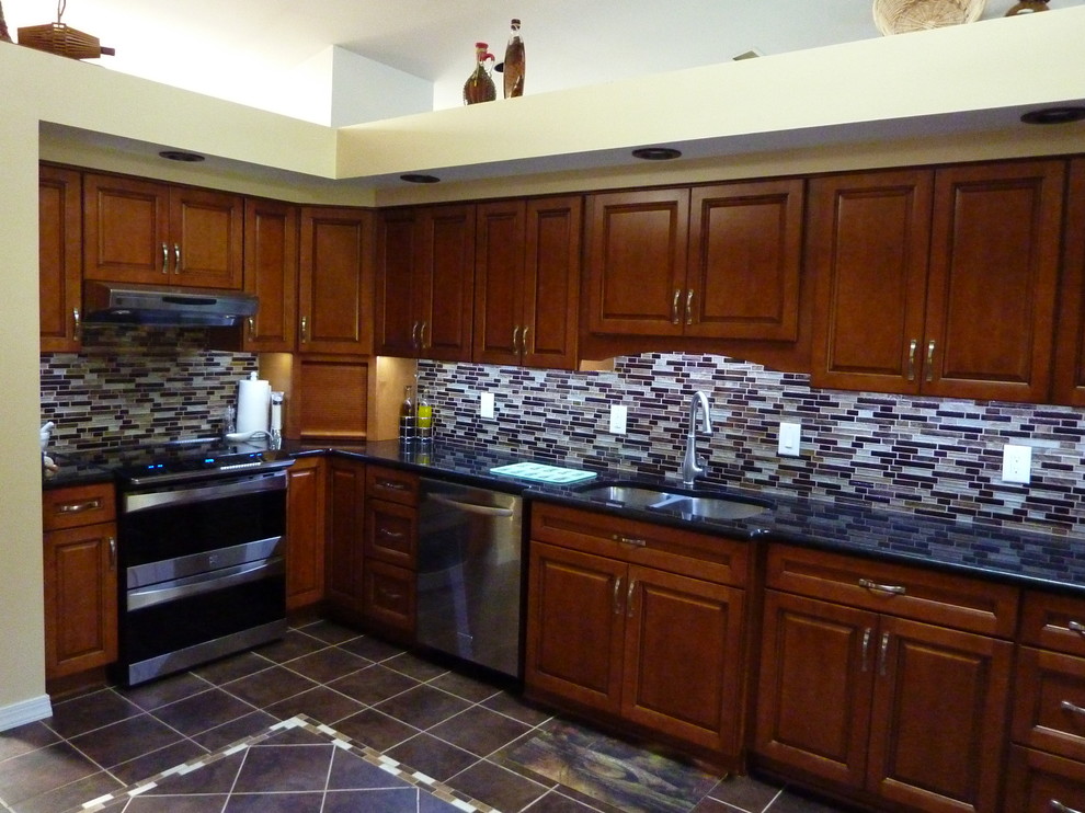Mid-sized elegant l-shaped porcelain tile and brown floor enclosed kitchen photo in Baltimore with a double-bowl sink, raised-panel cabinets, dark wood cabinets, granite countertops, multicolored backsplash, matchstick tile backsplash, stainless steel appliances, no island and black countertops