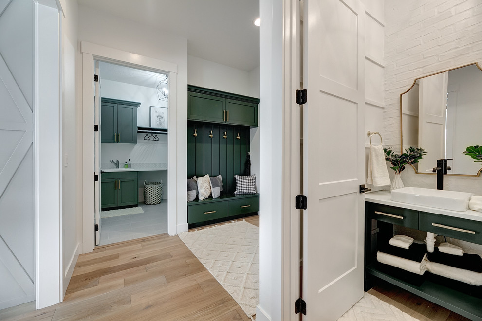 Photo of a mid-sized country powder room in Boise with furniture-like cabinets, green cabinets, a two-piece toilet, white walls, light hardwood floors, a vessel sink, solid surface benchtops, brown floor and white benchtops.