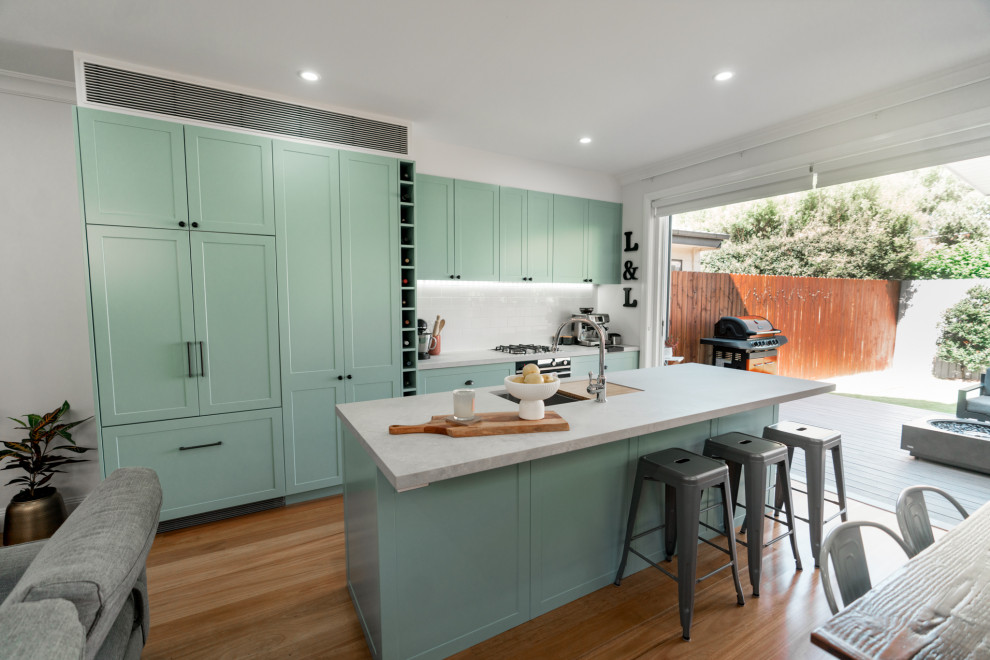 Inspiration for a mid-sized traditional galley eat-in kitchen in Sydney with an undermount sink, shaker cabinets, turquoise cabinets, quartz benchtops, white splashback, ceramic splashback, black appliances, light hardwood floors, with island, brown floor and grey benchtop.