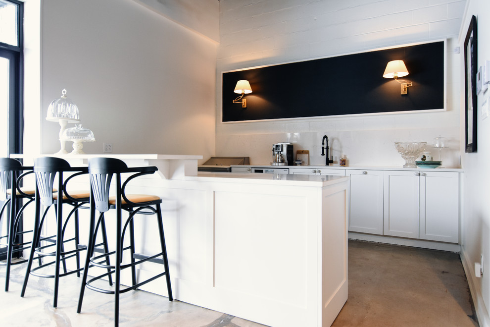 Example of a mid-sized transitional single-wall concrete floor and gray floor eat-in kitchen design with an undermount sink, shaker cabinets, white cabinets, quartz countertops, white backsplash, stone slab backsplash, white appliances and a peninsula