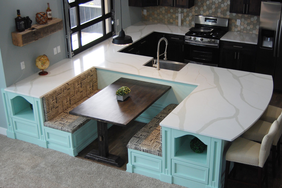 This is an example of an u-shaped kitchen in Grand Rapids with a farmhouse sink, dark wood cabinets, quartz benchtops, multi-coloured splashback, glass tile splashback, stainless steel appliances and a peninsula.