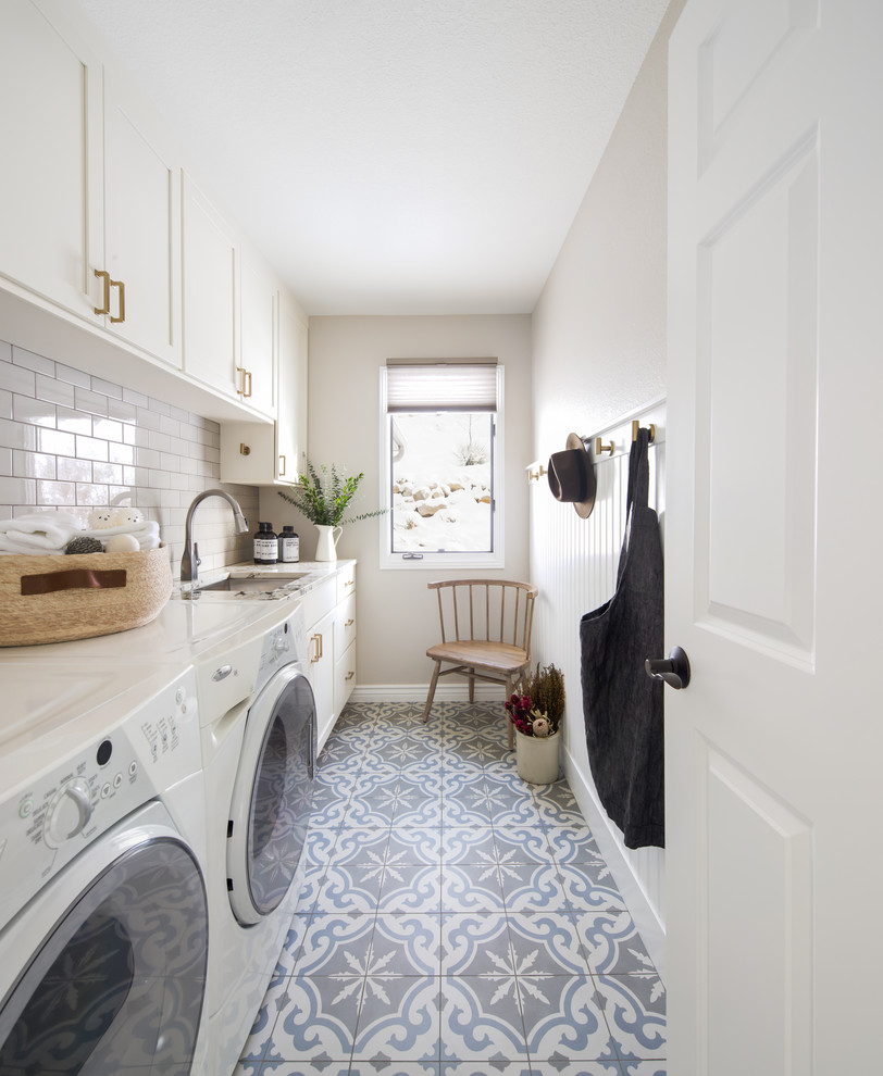 Photo of a mid-sized transitional galley dedicated laundry room in Denver with an undermount sink, recessed-panel cabinets, white cabinets, marble benchtops, white splashback, subway tile splashback, white walls, porcelain floors, a side-by-side washer and dryer, blue floor, white benchtop and planked wall panelling.