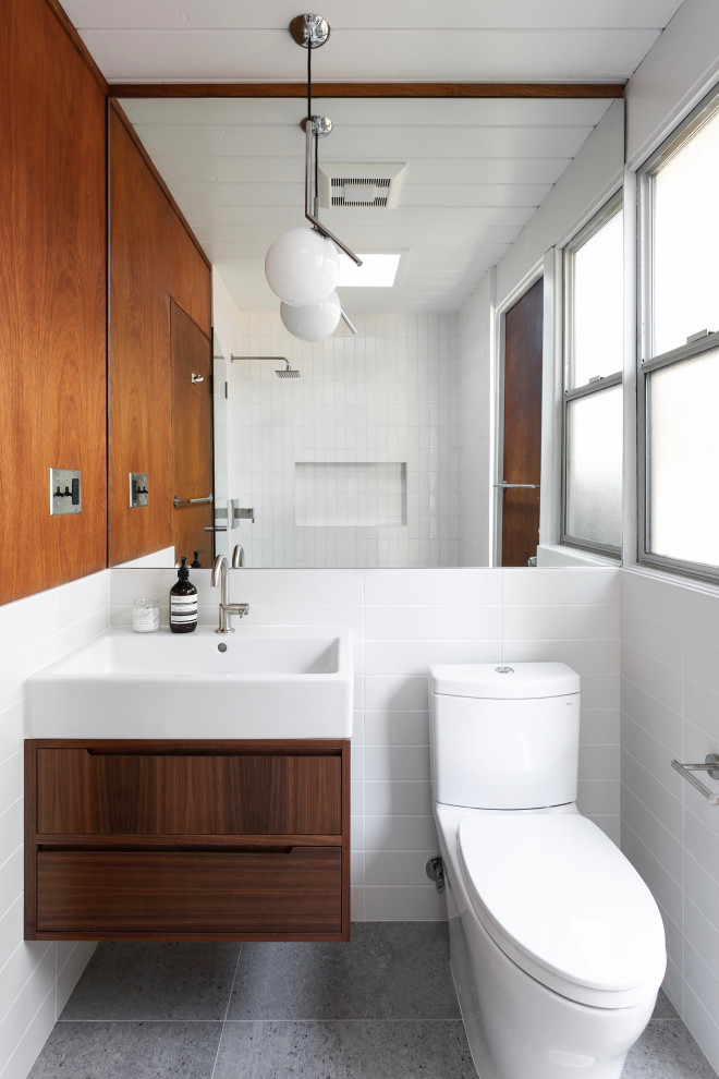 This is an example of a midcentury bathroom in San Francisco with flat-panel cabinets, dark wood cabinets, a two-piece toilet, white tile, white walls, a console sink, grey floor, a single vanity, a floating vanity, timber and wood walls.