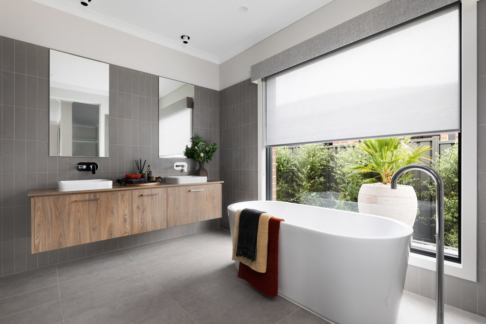 Photo of a contemporary master bathroom in Other with flat-panel cabinets, medium wood cabinets, a freestanding tub, gray tile, grey walls, a vessel sink, grey floor and brown benchtops.