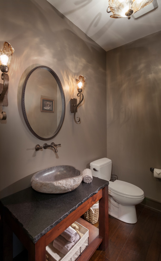 Inspiration for a mid-sized country powder room in Detroit with open cabinets, medium wood cabinets, a two-piece toilet, grey walls, a vessel sink, brown floor and grey benchtops.