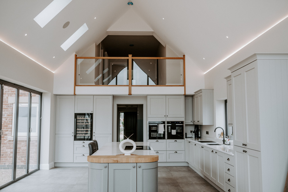 This is an example of a large traditional kitchen with a submerged sink, shaker cabinets, grey cabinets, quartz worktops, black appliances, porcelain flooring, an island, white worktops and a vaulted ceiling.