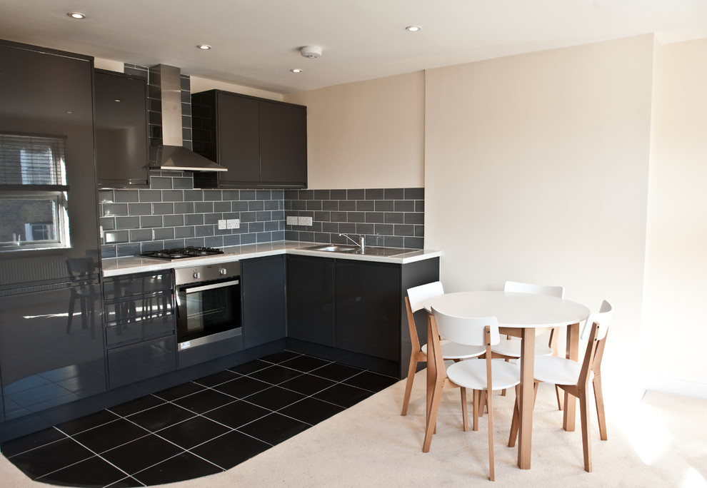 This is an example of a large modern single-wall open plan kitchen in London with a drop-in sink, flat-panel cabinets, black cabinets, quartz benchtops, grey splashback, ceramic splashback, stainless steel appliances, ceramic floors and no island.