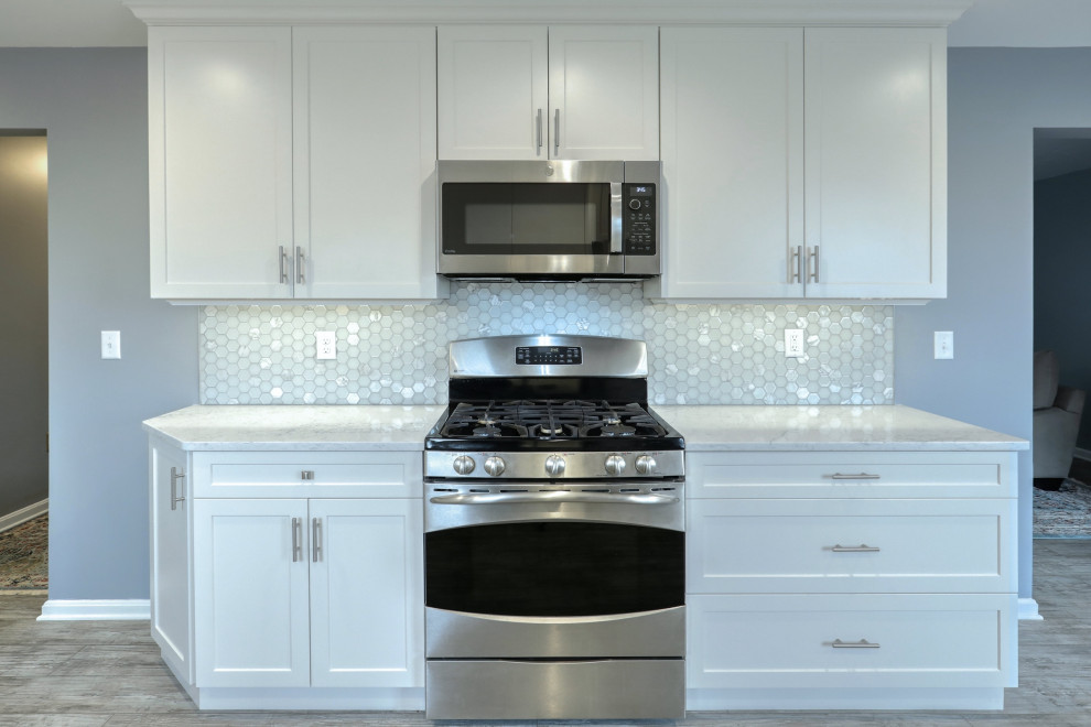 Example of a mid-sized transitional vinyl floor and gray floor eat-in kitchen design with an undermount sink, shaker cabinets, white cabinets, quartz countertops, gray backsplash, glass tile backsplash, stainless steel appliances, no island and white countertops