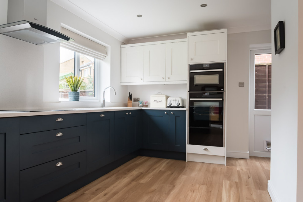 Design ideas for a mid-sized traditional u-shaped eat-in kitchen in Berkshire with a double-bowl sink, shaker cabinets, blue cabinets, quartzite benchtops, white splashback, black appliances, linoleum floors, a peninsula, brown floor and white benchtop.