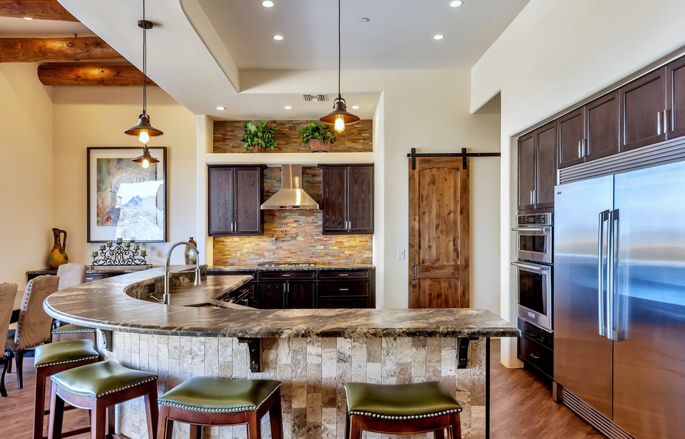 Photo of an u-shaped kitchen in Phoenix with an undermount sink, recessed-panel cabinets, dark wood cabinets, stainless steel appliances, medium hardwood floors, with island, brown floor and black benchtop.