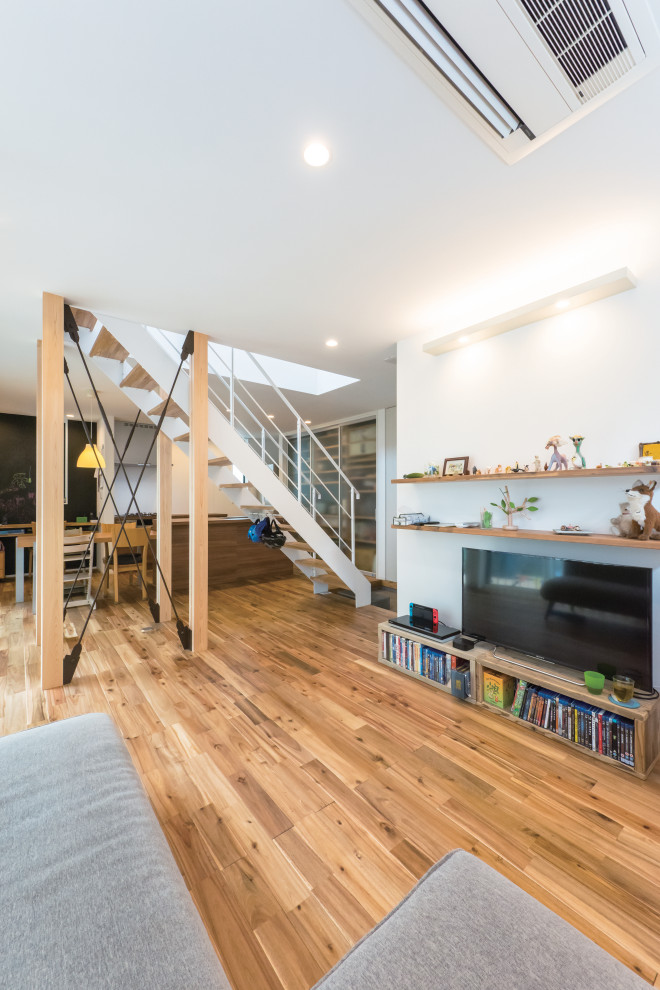 This is an example of a mid-sized industrial formal open concept living room in Tokyo Suburbs with white walls, medium hardwood floors, a freestanding tv and brown floor.