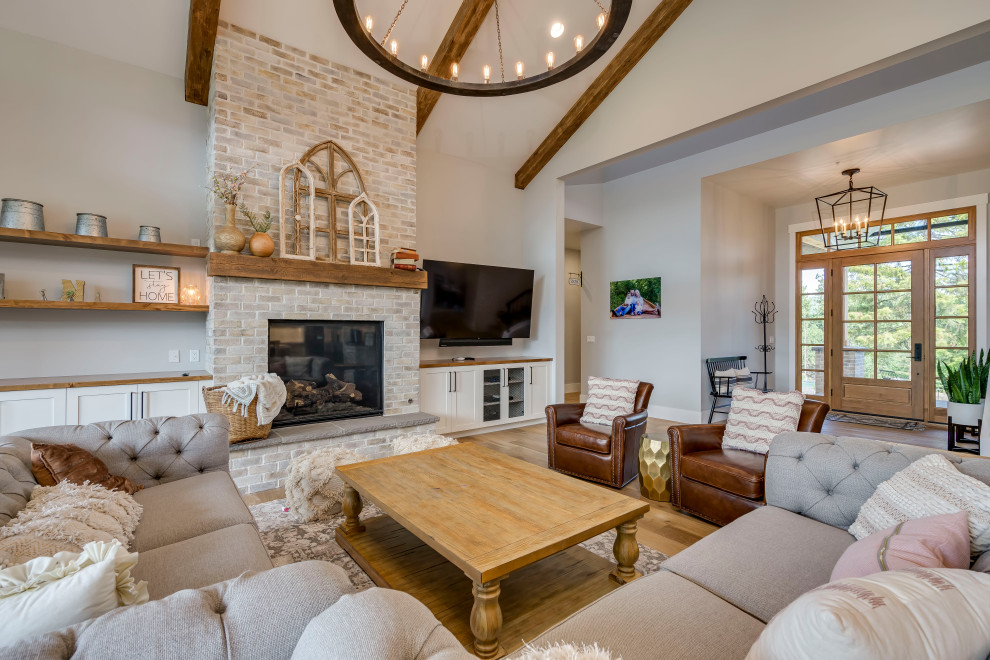 This is an example of a transitional open concept living room in Other with white walls, medium hardwood floors, a standard fireplace, a brick fireplace surround, a wall-mounted tv, brown floor and exposed beam.