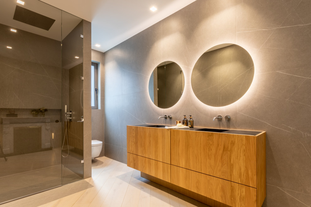 This is an example of a large contemporary 3/4 bathroom in Madrid with flat-panel cabinets, medium wood cabinets, an alcove shower, gray tile, an integrated sink, beige floor, a hinged shower door, black benchtops, a double vanity and a built-in vanity.