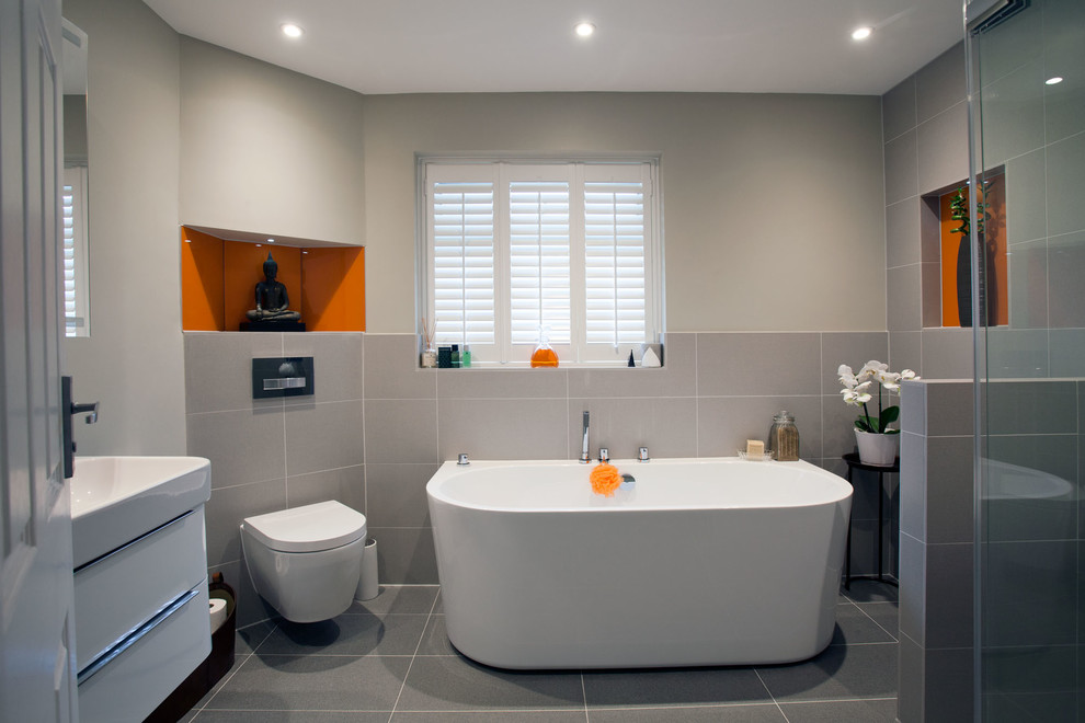 This is an example of a mid-sized modern kids bathroom in Sussex with furniture-like cabinets, grey cabinets, a freestanding tub, an open shower, a one-piece toilet, grey walls, ceramic floors, an integrated sink, grey floor and an open shower.