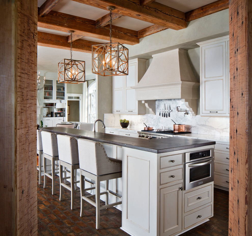 This is an example of a large traditional l-shaped open plan kitchen in New Orleans with a farmhouse sink, beaded inset cabinets, white cabinets, marble benchtops, white splashback, stone slab splashback, panelled appliances, brick floors and with island.