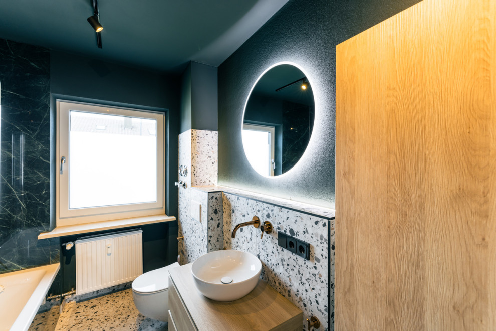 This is an example of a small contemporary bathroom in Munich with flat-panel cabinets, brown cabinets, a built-in bath, a wall mounted toilet, multi-coloured tiles, marble tiles, green walls, terrazzo flooring, a vessel sink, wooden worktops, white floors, a hinged door, brown worktops, a single sink and a floating vanity unit.